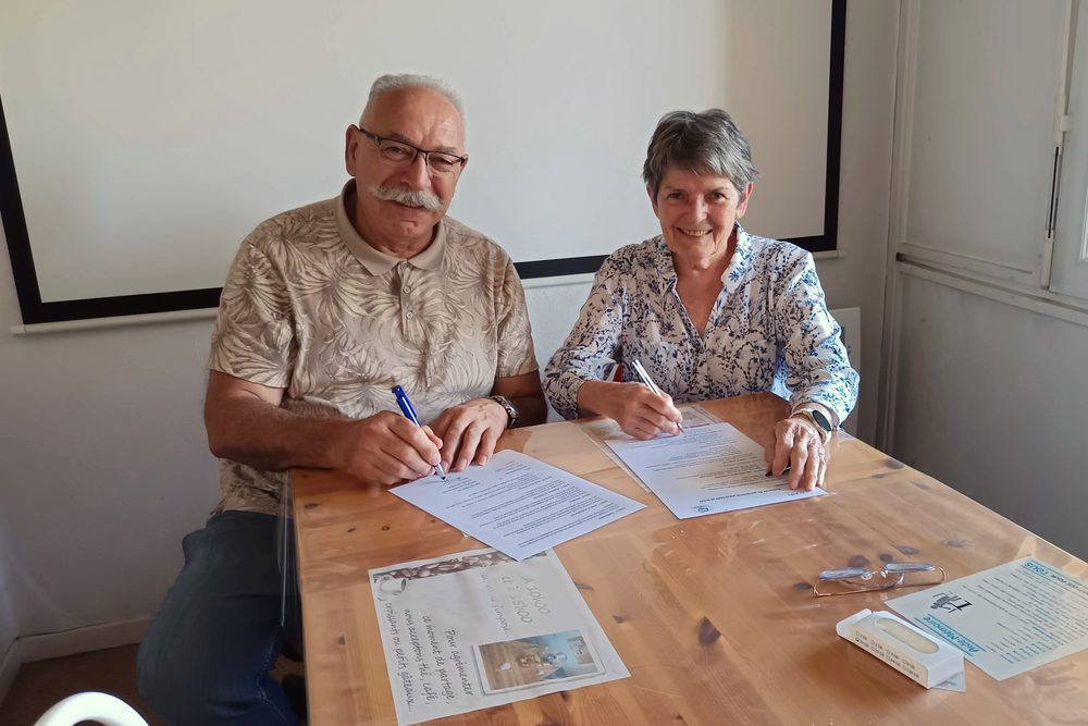 Deux personnes assises à une table signent chacune un exemplaire de la convention de partenariat entre le club et l’AIFI Nord-Isère
